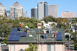 工人们在奥克兰市中心附近的一所房子上安装太阳能电池板，这是一个利用加州限额交易拍卖收入的项目。